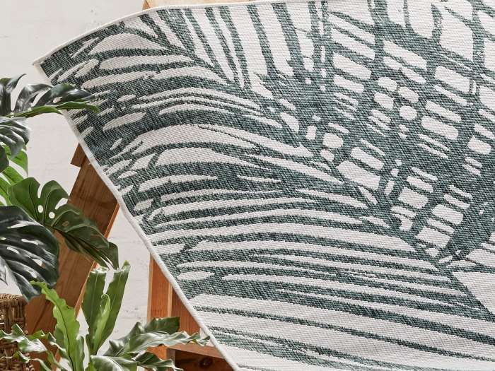 close up of palm reversible outdoor rug on palettes with plants